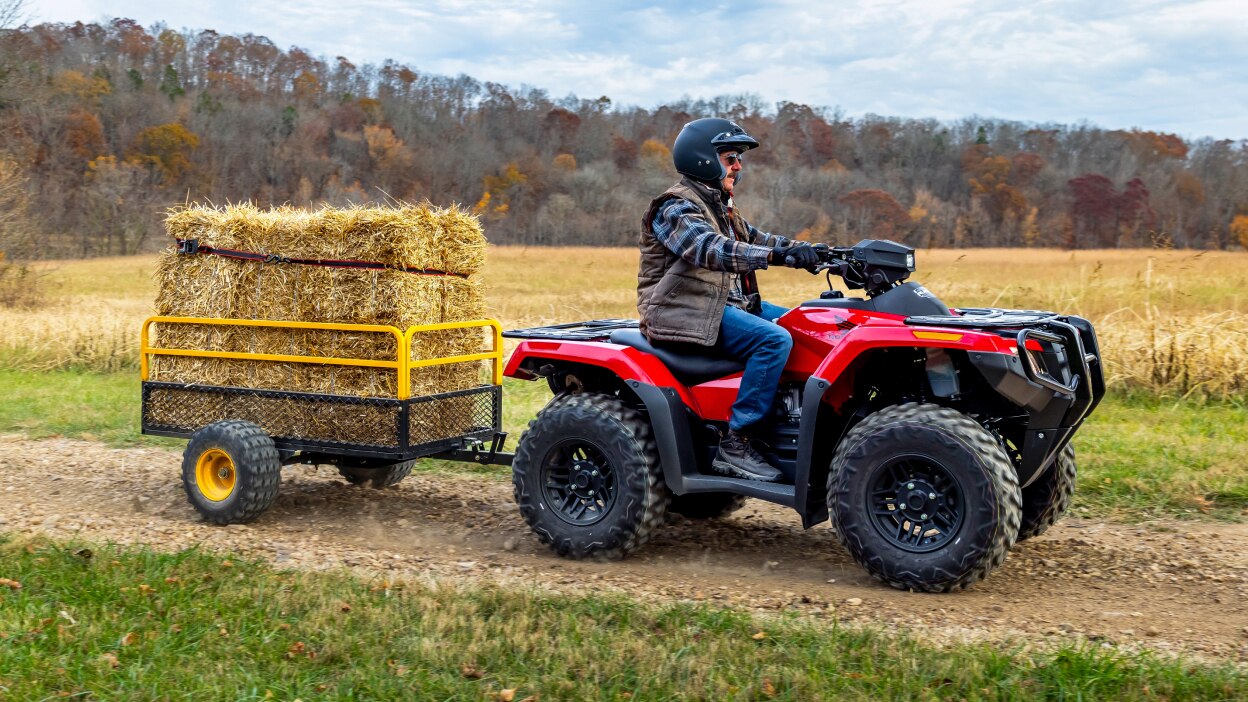 A rider pulling a trailer with hay on a Honda Rubicon 700 