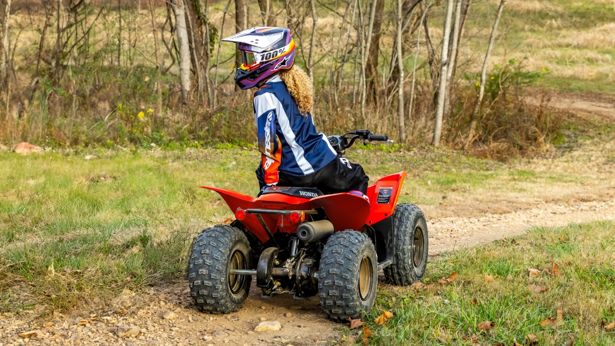 Rear view of young rider on ATV in Field.
