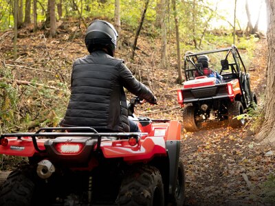 Riders in a Honda SxS and a on a Honda ATV riding on a trail in safety gear 