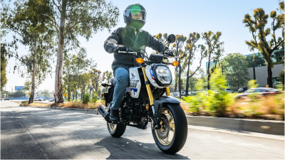 Rider on yellow bike at slight right angle driving through street. Small bushes and trees in background.