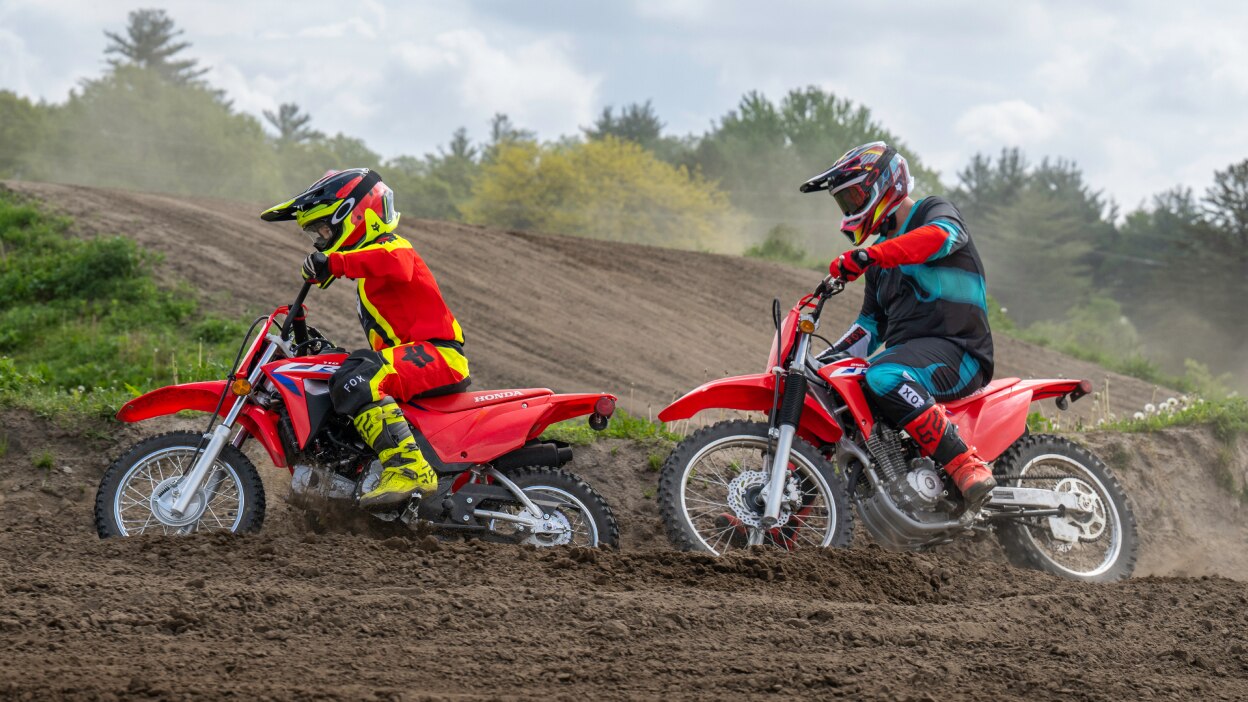 Young rider in front of adult rider on dirt track.