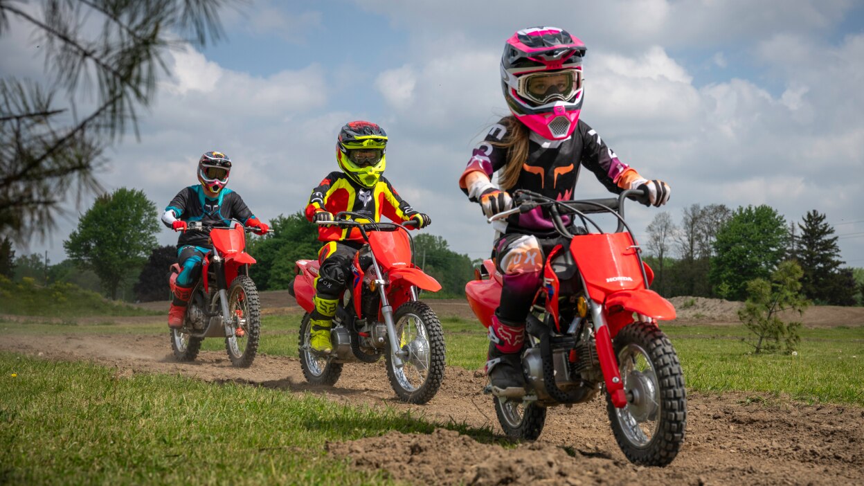 Two young riders in front of adult rider on dirt track.