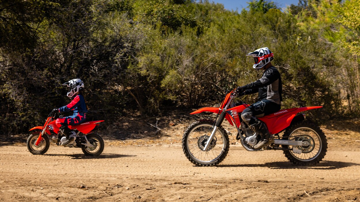 One young rider in front of adult rider, going left. Left angle.