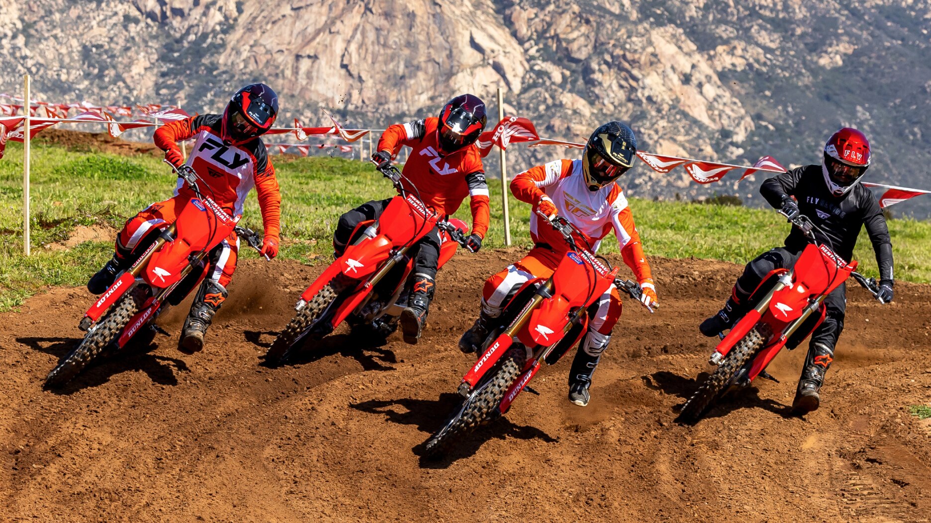 Four riders turning left on dirt track. Front facing.