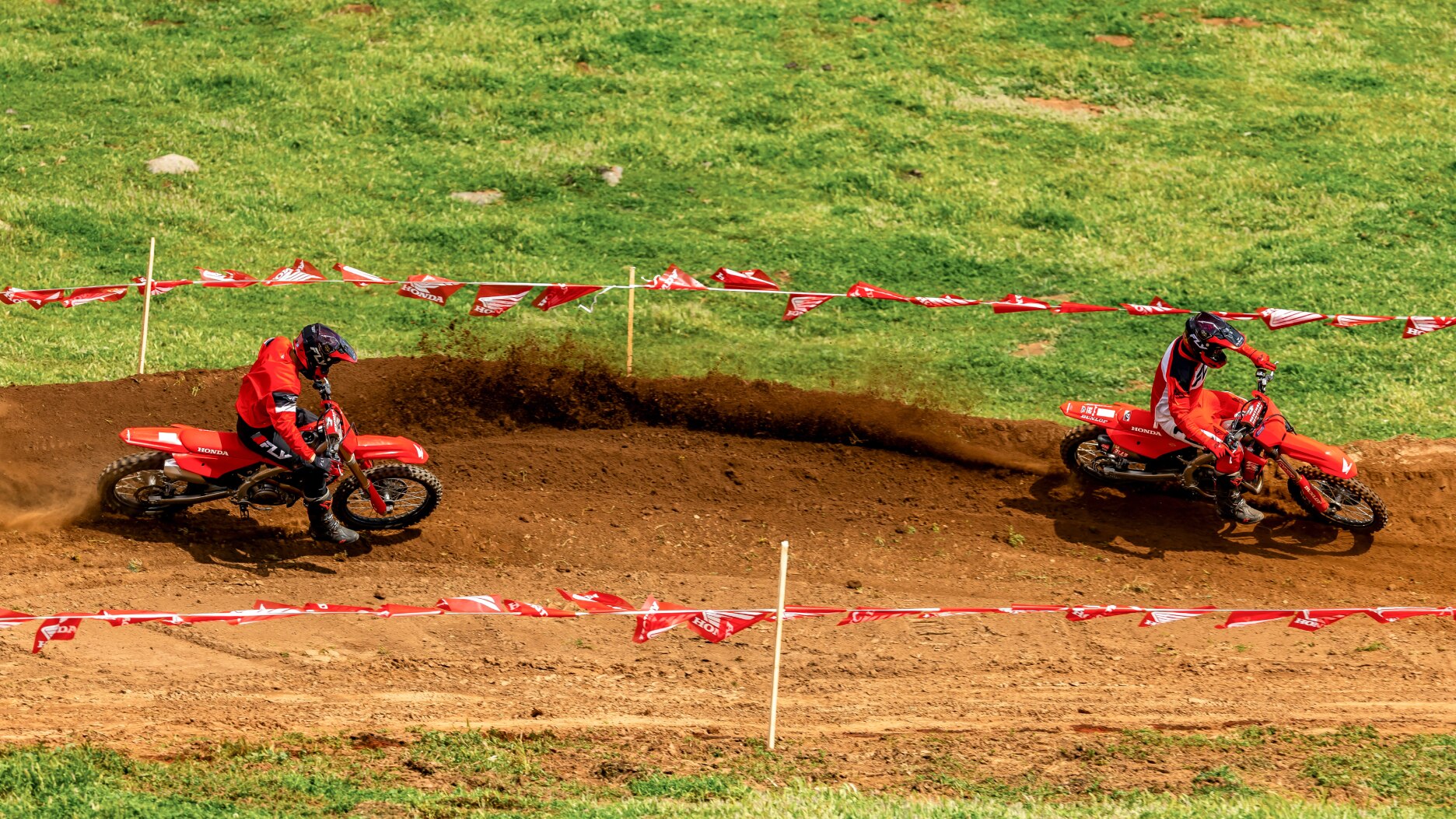 Two riders on dirt track, facing right. one on each side of image.