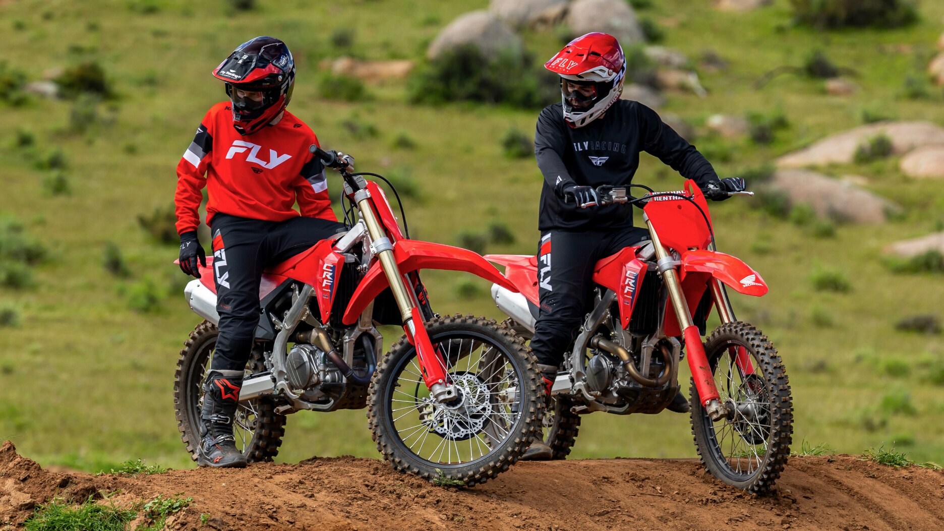 Two riders on hill, not moving, looking to their right.