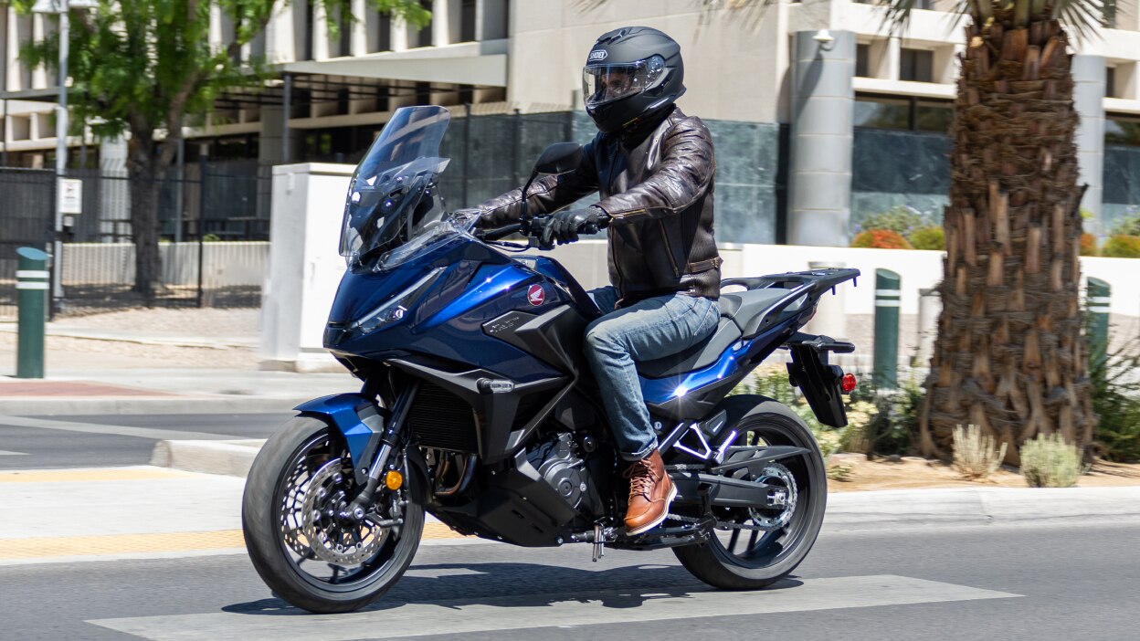 Rider facing left on NT1100. City landscape in background.