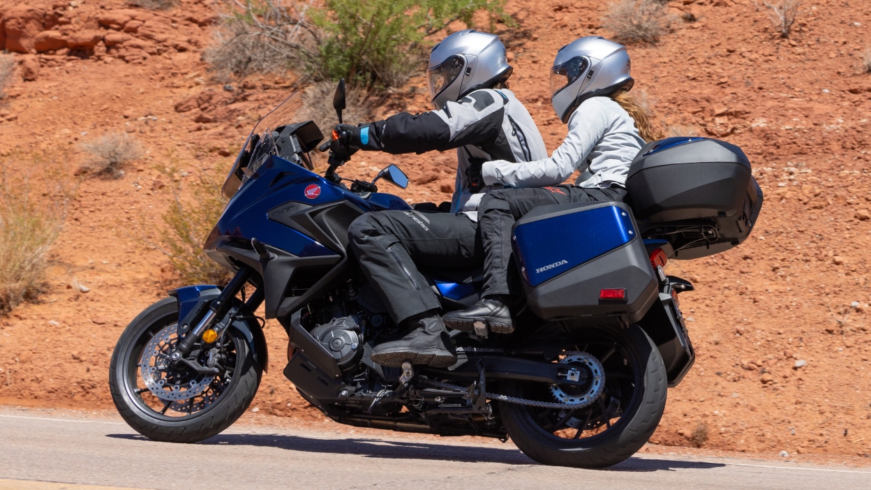 Rider and passenger facing left on NT1100. Desert landscape in background.