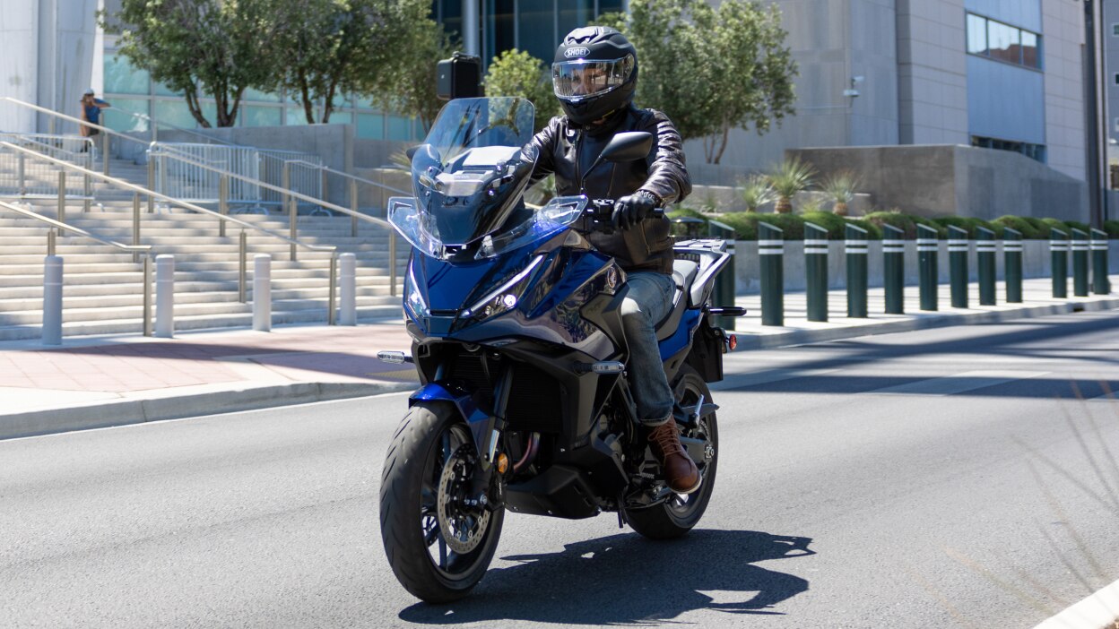 Rider facing left on NT1100. City landscape in background.