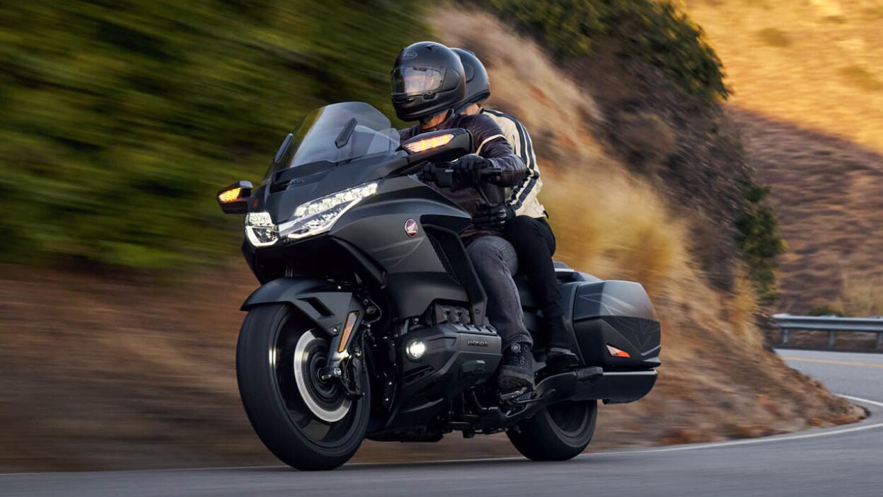 Front angle of rider and passenger on Gold Wing on road. Mountain background.