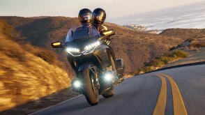Front angle of rider and passenger on Gold Wing on road. Mountain background.