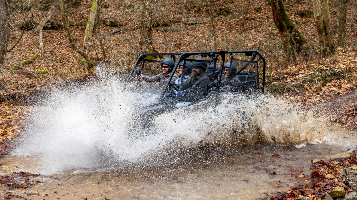 Four people in sxs going left into puddle.