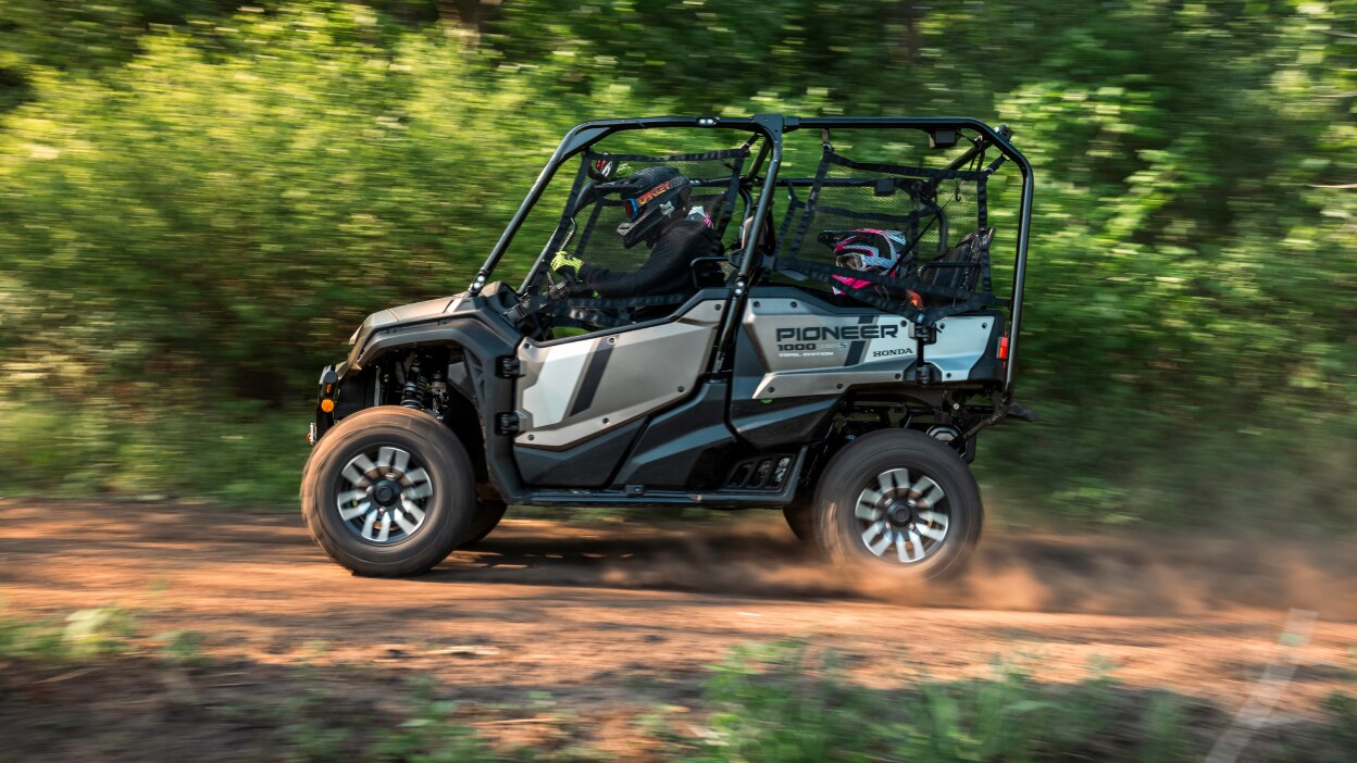 Two people in grey sxs going right. Green field background.