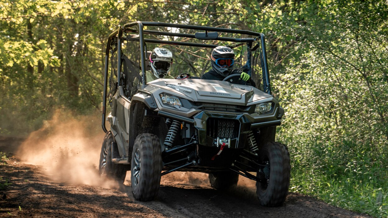 Two people with helmets in sxs going right. Greenary background.